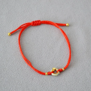 Close-up of red braided rope bracelet with golden beads and enamel dragon charm