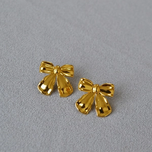 Detail of gold bow earrings with hammer texture finish on grey fabric background