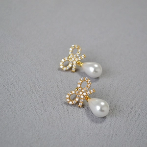 Detail of bow-shaped zircon earrings with elegant white teardrop pearl pendants