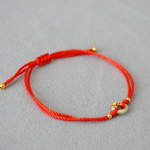 Detail of red woven bracelet featuring gold beads and a jade-like round pendant