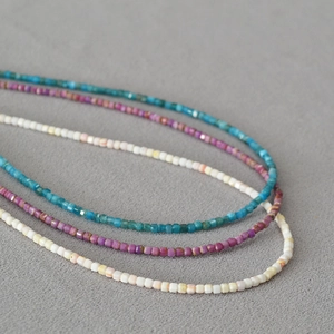 Détail macro de colliers perlés à la main avec pierres carrées bleues, magenta et blanches