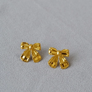 Close-up of golden bow-shaped stud earrings with a 3D pleated metal texture design