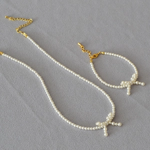 Detailed close-up of pearl necklace and bracelet set with elegant bow design and gold clasp