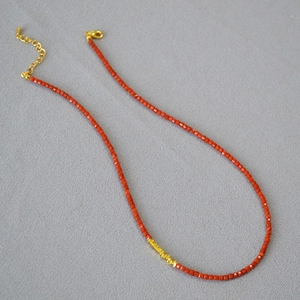Flat lay of red agate beaded necklace with gold accents and clasp on dark textured background