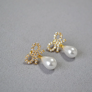 Macro shot of gold bow stud earrings featuring sparkling zircon and a white teardrop pearl