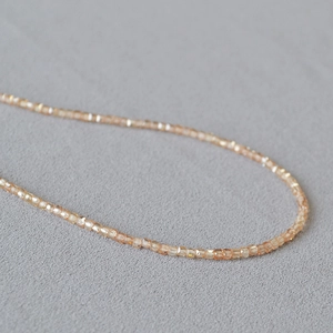 Macro view of champagne faceted crystal beads on a minimalist necklace on grey fabric