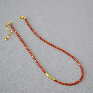 Close-up of red agate beaded necklace with faceted stone beads and gold cylinder spacers