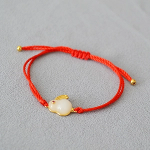 Detail of red braided zodiac bracelet featuring a white rabbit pendant with gold edging