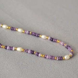 Detailed macro view of purple amethyst stones, rice pearls, and golden spacer beads