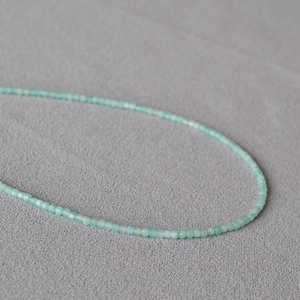 Makroaufnahme winziger 2mm facettierter hellblauer Natursteinperlen an einer Kette