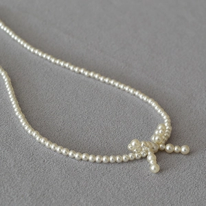 Elegant white pearl choker necklace featuring a unique side bow design on grey fabric