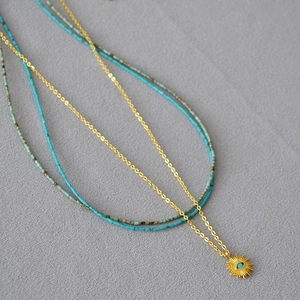 Détail d'un collier doré à plusieurs rangs avec pendentif soleil et perles turquoise sur tissu