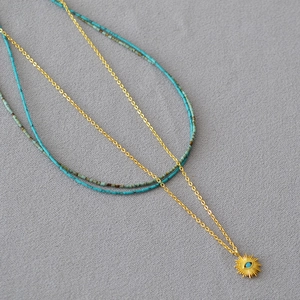 Détail d'un collier doré multicouche avec pendentif œil solaire et perles turquoise
