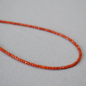 Macro view of tiny faceted orange-red agate cube beads on a minimalist necklace