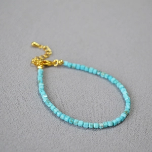 Dettaglio di bracciale con perline quadrate blu e catena regolabile dorata con ciondolo