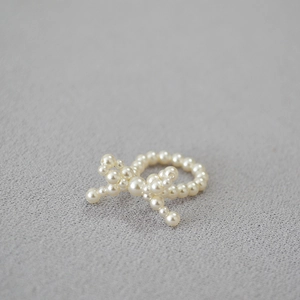 Elegante anello a fiocco con perle intrecciate in bianco crema su fondo grigio