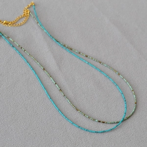 Gros plan d'un collier double rang avec perles turquoise et marron sur tissu texturé gris