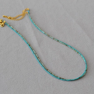 Collier double épaisseur en perles de turquoise avec fermoir doré sur fond de tissu gris