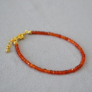 Macro shot of faceted orange agate beads with gold plated lobster clasp on a felt surface