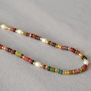 Detail of colorful beads and pearls necklace with gold spacers on grey fabric