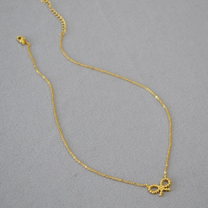 Collier avec pendentif nœud en laiton plaqué or sur un fond texturé gris haut de gamme