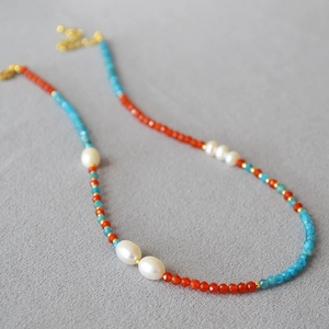Détail d'un collier en perles avec agate rouge, apatite bleue et perles sur tissu gris
