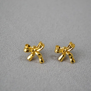 Elegant gold-plated brass bow earrings with 925 silver needle on a grey texture