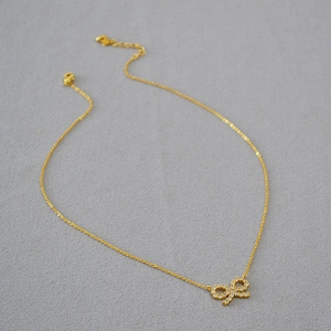 Vue macro du collier avec pendentif nœud doré et zircons sur fond de tissu gris texturé