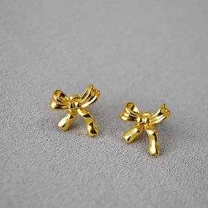 Minimalist gold bow stud earrings with polished ribbon design on textured grey backdrop