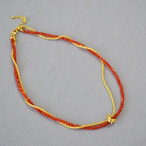 Detail of red agate beads and golden textured knot on a double-layer necklace chain