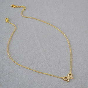 Gros plan d'un pendentif nœud doré serti de zircons avec une fine chaîne en O