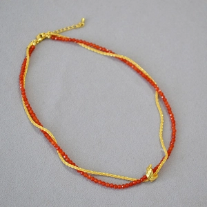 Detail of double-layer necklace with red beads, gold knot pendant and lobster clasp