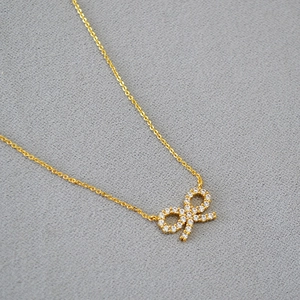 Collier doré avec pendentif nœud et pavé de zircons blancs sur tissu gris chiné