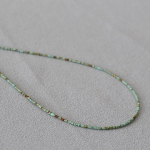 Détail d'un collier de perles turquoise minimaliste posé sur un tissu en lin rustique