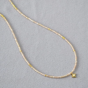 Détail du collier de perles avec pendentif étoile en zircon champagne sur tissu sombre