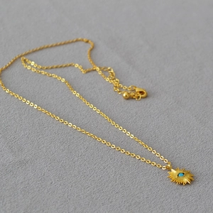 Collier minimaliste à pendentif soleil doré avec une pierre turquoise sur feutre gris