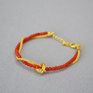 Detail of double-layer necklace with red faceted beads, gold chain and knot pendant