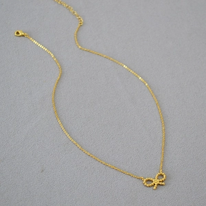 Gros plan du pendentif nœud doré avec texture de micro-perles sur une chaîne fine