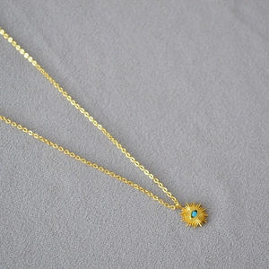 Détail macro du pendentif soleil doré avec œil turquoise sur une chaîne fine