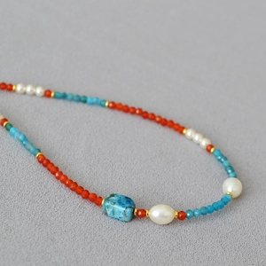 Detailed close-up of beaded necklace with blue agate, pearls and orange apatite stones