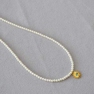 Détail d'un collier de perles blanches avec pendentif soleil doré et turquoise bleue