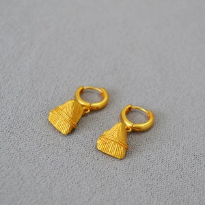 Macro detail of gold brass earrings featuring textured conical pendants on felt