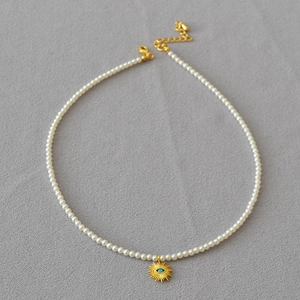 Détail d'un collier de perles fines avec pendentif soleil doré et perle œil bleu porte-bonheur
