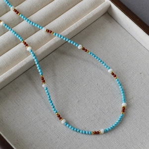 Artistic handmade beaded necklace with turquoise and shell beads on a grey linen tray