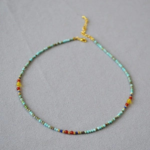 Ethnic style necklace with turquoise beads and colorful stone accents on grey background