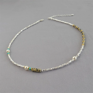 Collier minimaliste en perles argentées avec perles blanches et turquoise sur fond gris