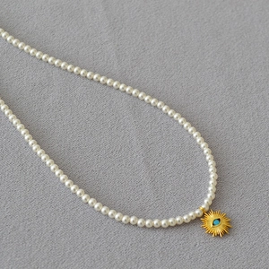 Détail du pendentif œil turquoise et perles blanches sur collier minimaliste chic