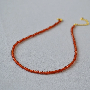 Macro shot of faceted red agate beads on a minimalist necklace with gold clasp