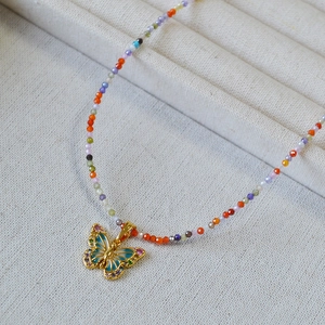 Détail d'un collier de perles colorées avec pendentif papillon en émail bleu sur plateau