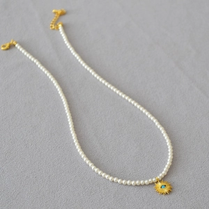 Détail du collier de perles blanches avec pendentif soleil doré et charme œil bleu